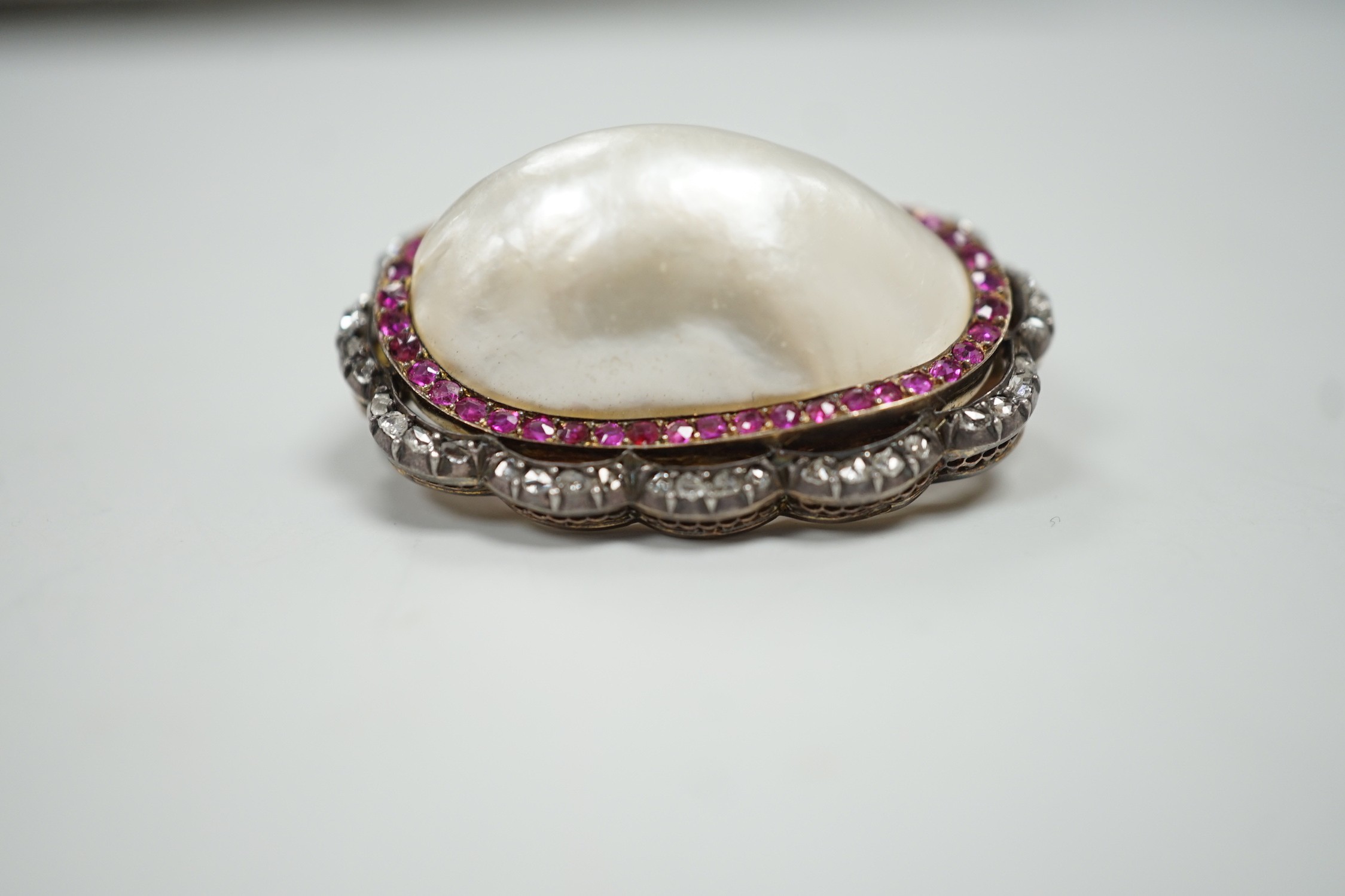 An early 20th century French yellow metal (18ct poincon mark on pin), white metal and mabe pearl set oval brooch, bordered by concentric rows of rubies and rose cut diamonds, 38mm, gross weight 17.3 grams.